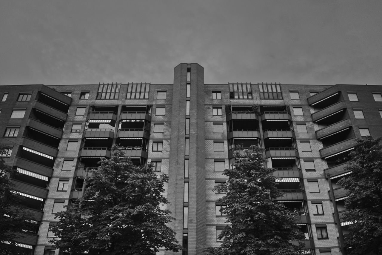 Black and white photo of a modern apartment building facade with trees.