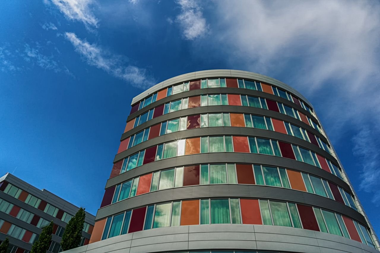 A modern curved building with colorful panels against a blue sky, showcasing urban architecture.