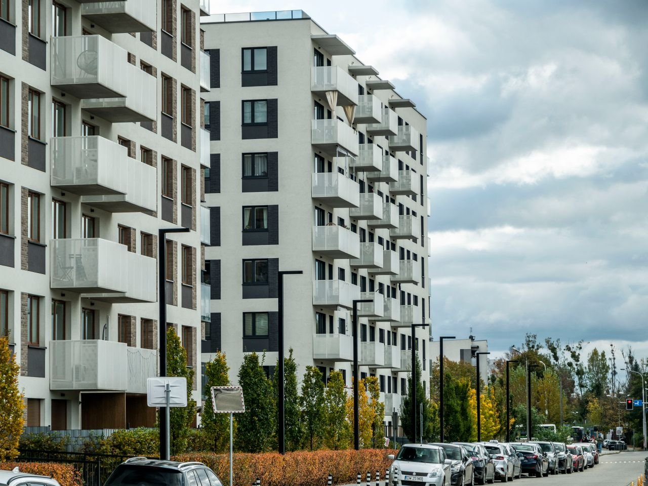 Contemporary apartment complex on a city street lined with parked cars and autumn foliage.
